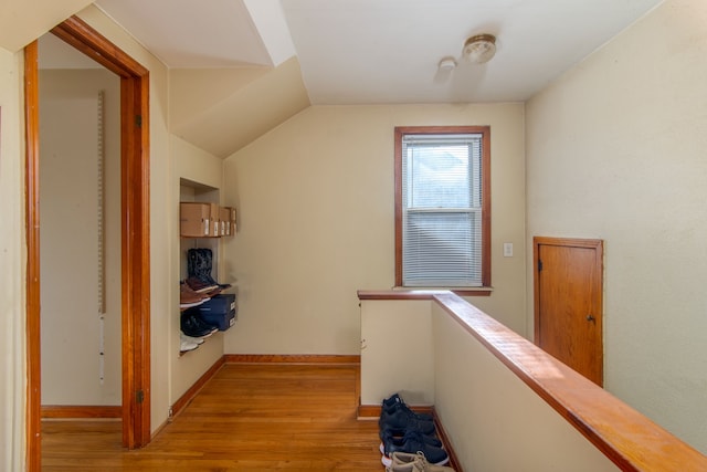 hall with an upstairs landing, baseboards, vaulted ceiling, and light wood finished floors