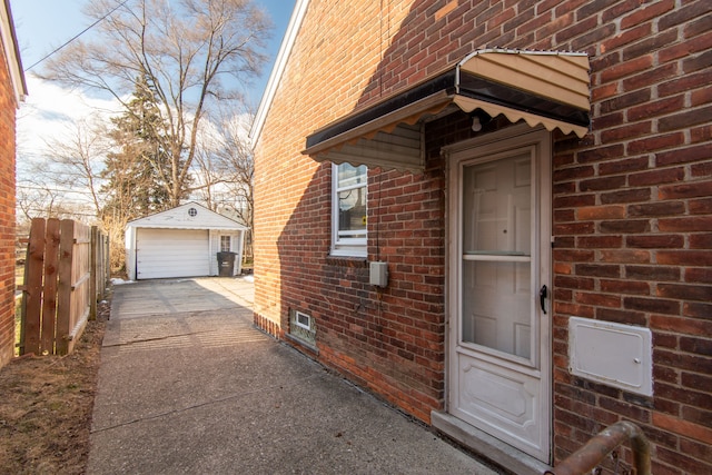 doorway to property featuring driveway, a detached garage, fence, and brick siding