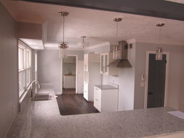 kitchen featuring wall chimney range hood, a sink, and decorative light fixtures