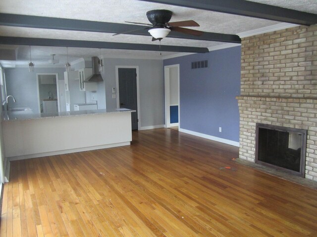 unfurnished living room with baseboards, visible vents, wood finished floors, beamed ceiling, and a brick fireplace