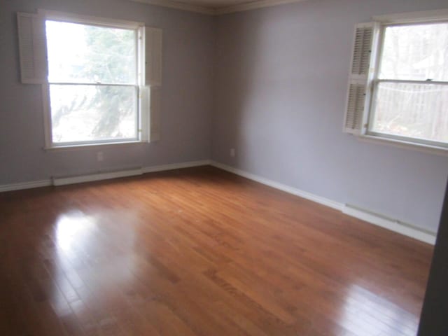 spare room featuring crown molding, baseboard heating, wood finished floors, and baseboards