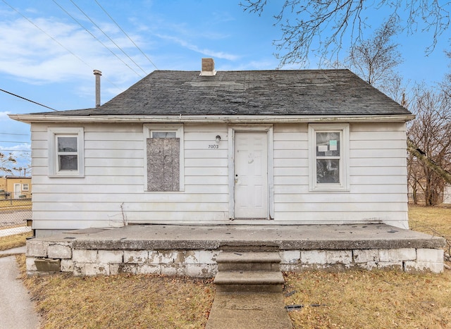 rear view of house featuring a chimney, fence, and roof with shingles