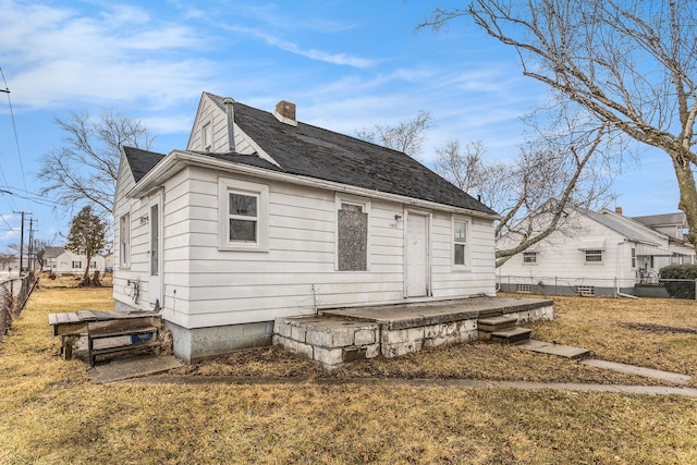 rear view of house featuring a shingled roof, a chimney, fence, and a yard