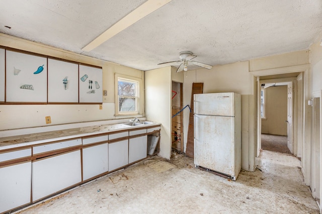 kitchen with a ceiling fan, freestanding refrigerator, light countertops, white cabinetry, and a sink