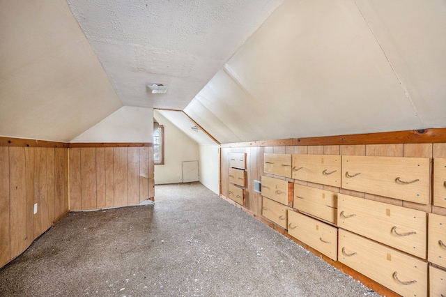 bonus room with wood walls, vaulted ceiling, and a textured ceiling