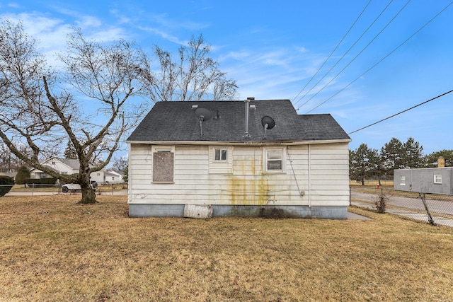 back of property with a yard, a shingled roof, and fence