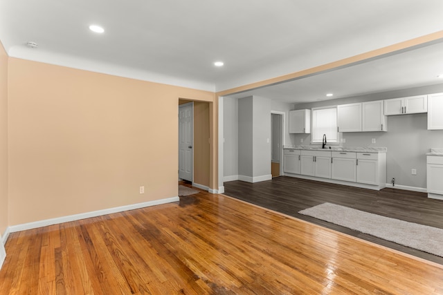 unfurnished living room featuring recessed lighting, dark wood-style flooring, a sink, and baseboards