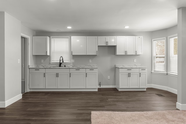 kitchen featuring white cabinetry, light stone counters, and a sink