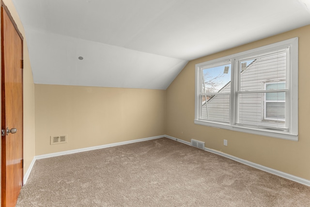 additional living space with light colored carpet, visible vents, lofted ceiling, and baseboards