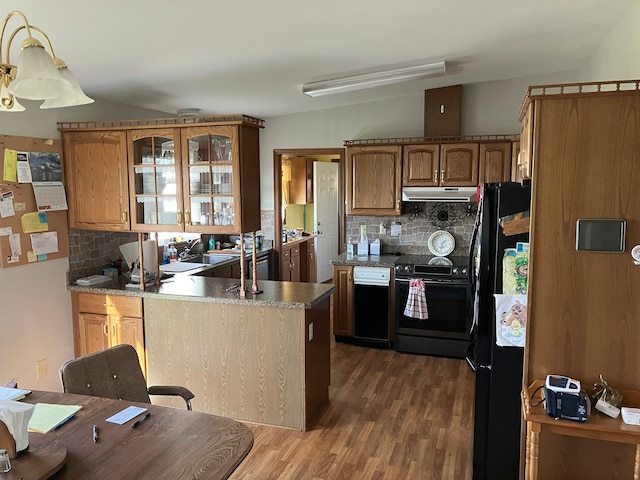 kitchen featuring lofted ceiling, a peninsula, wood finished floors, under cabinet range hood, and black appliances