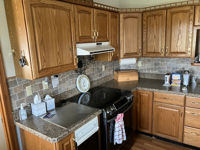 kitchen featuring decorative backsplash, dark countertops, brown cabinets, under cabinet range hood, and black range with electric cooktop