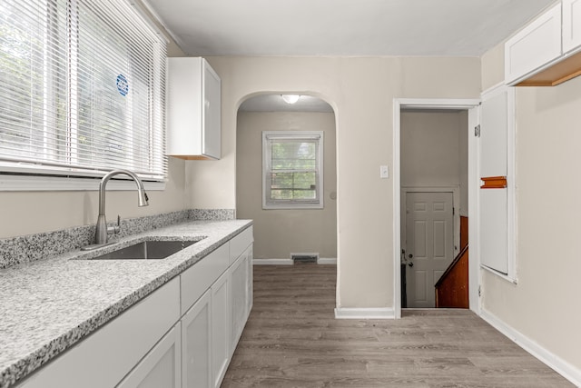 kitchen with arched walkways, a sink, baseboards, white cabinets, and light wood finished floors