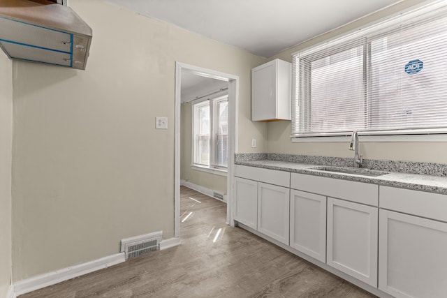 kitchen with a sink, visible vents, white cabinets, baseboards, and light wood-type flooring