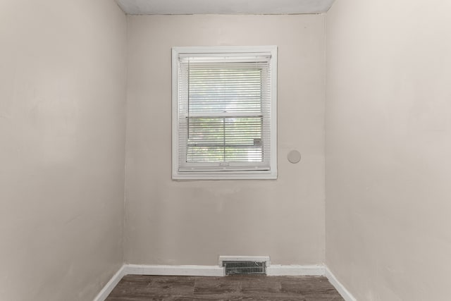 empty room with dark wood-style flooring, visible vents, and baseboards