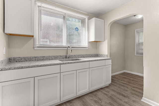 kitchen featuring arched walkways, light wood finished floors, light countertops, a sink, and baseboards