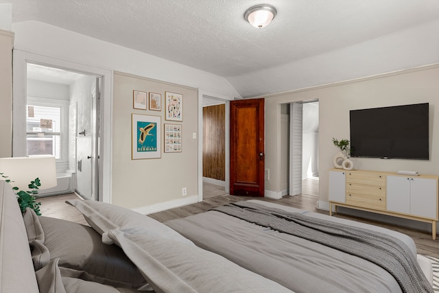 bedroom featuring lofted ceiling, ensuite bathroom, a textured ceiling, wood finished floors, and baseboards