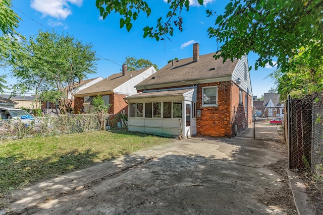 rear view of house with a sunroom, a chimney, a gate, fence, and brick siding