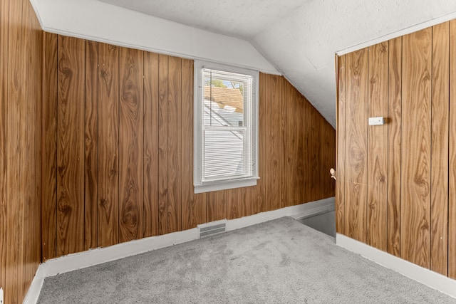 additional living space with visible vents, vaulted ceiling, a textured ceiling, carpet flooring, and wood walls