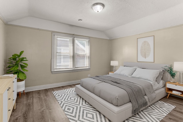 bedroom featuring vaulted ceiling, a textured ceiling, baseboards, and wood finished floors