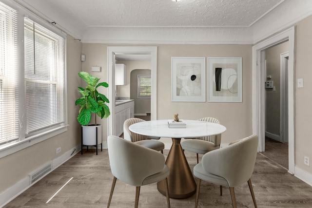 dining room with arched walkways, light wood finished floors, visible vents, and a healthy amount of sunlight