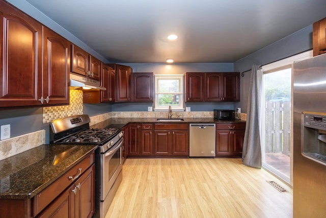 kitchen with under cabinet range hood, a sink, visible vents, appliances with stainless steel finishes, and dark stone counters