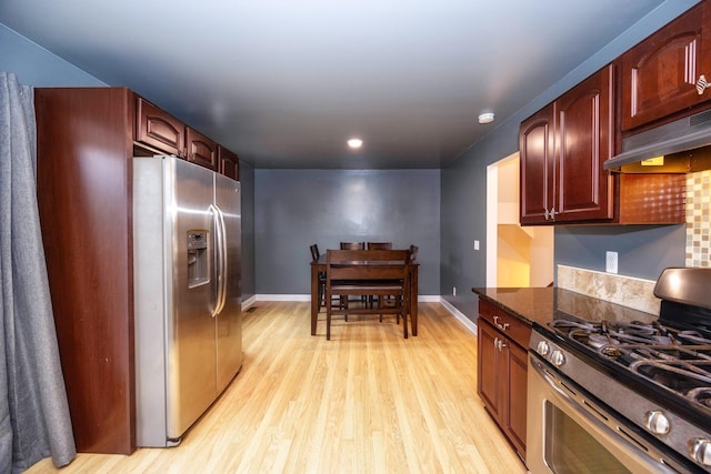 kitchen featuring under cabinet range hood, stainless steel appliances, baseboards, light wood-style floors, and dark stone counters