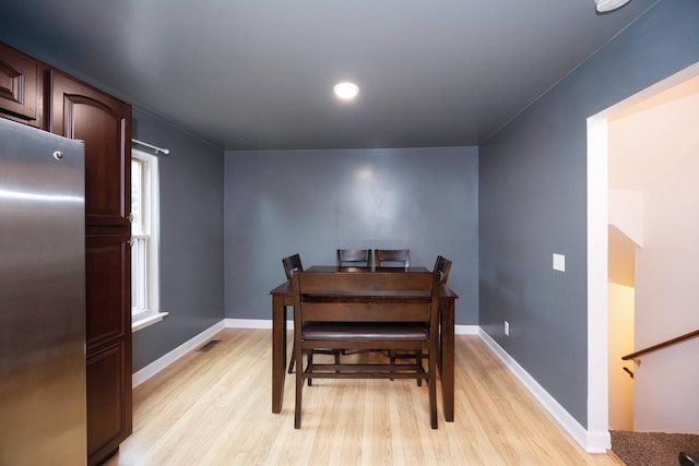 dining area with light wood-type flooring, visible vents, and baseboards