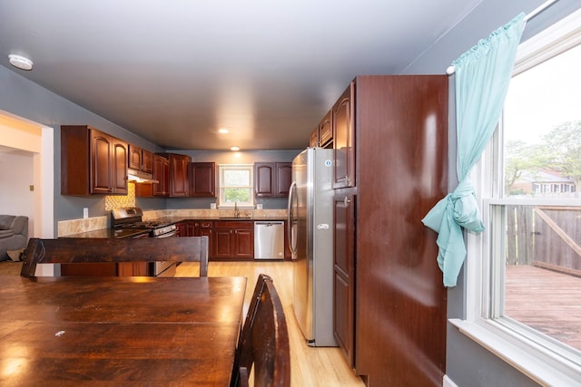 kitchen with stainless steel appliances, dark countertops, light wood-style floors, a sink, and under cabinet range hood