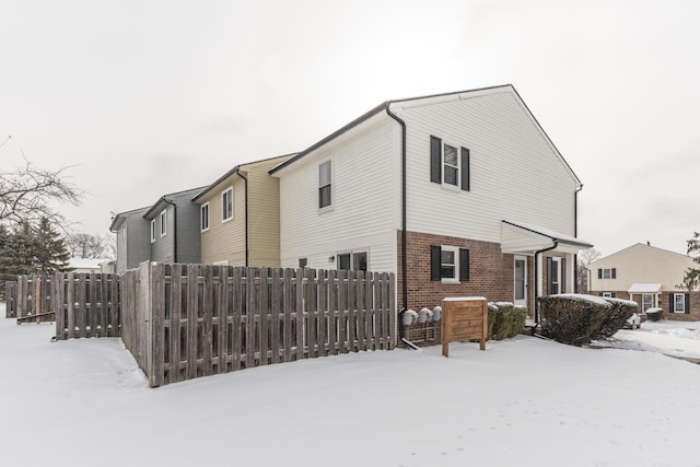 view of snowy exterior featuring brick siding and fence