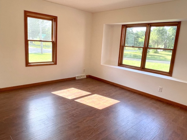 empty room with dark wood-style flooring, plenty of natural light, and visible vents