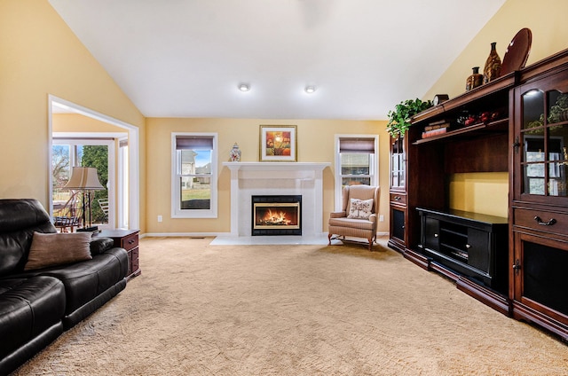 living area with a fireplace with flush hearth, a wealth of natural light, vaulted ceiling, and carpet floors