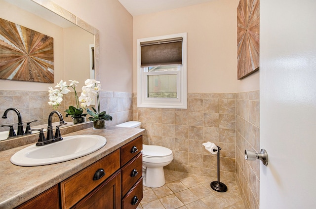 bathroom featuring tile patterned flooring, toilet, a wainscoted wall, vanity, and tile walls