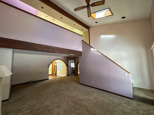 unfurnished living room featuring arched walkways, a ceiling fan, beamed ceiling, carpet floors, and high vaulted ceiling