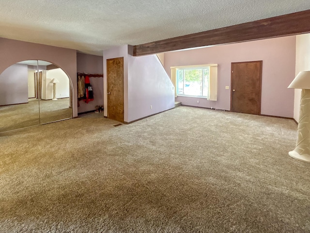 carpeted spare room with arched walkways, visible vents, a textured ceiling, and baseboards