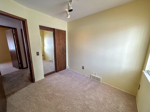 unfurnished bedroom featuring rail lighting, a closet, visible vents, and carpet flooring