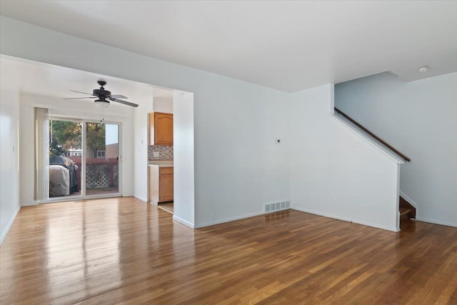 unfurnished living room with ceiling fan, dark wood-type flooring, stairway, and visible vents