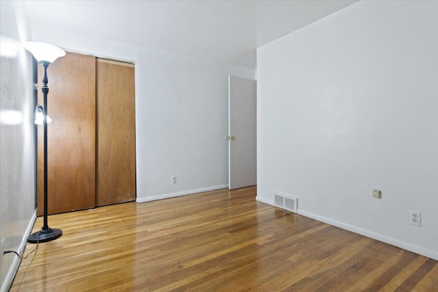 unfurnished bedroom with baseboards, a closet, visible vents, and wood finished floors