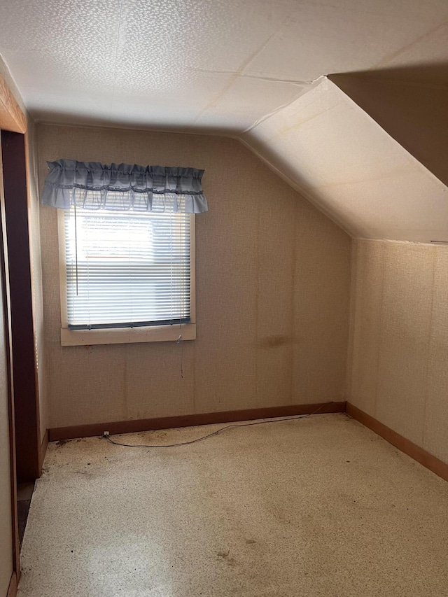 bonus room with lofted ceiling, a textured ceiling, and baseboards