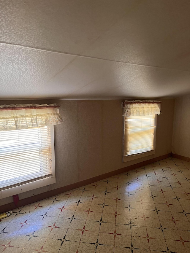 unfurnished room featuring a healthy amount of sunlight, light floors, baseboards, and a textured ceiling