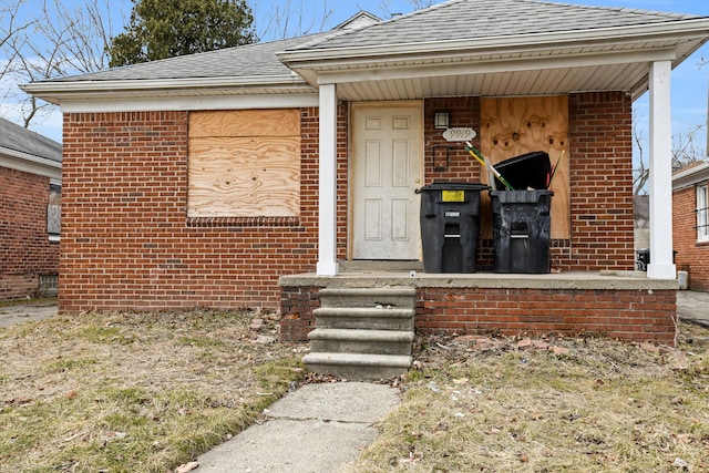 doorway to property featuring brick siding and a shingled roof