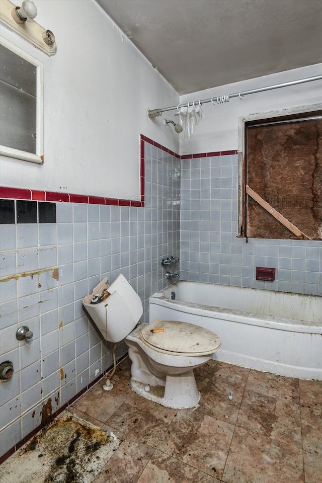 bathroom with a wainscoted wall, toilet, tile walls, and washtub / shower combination