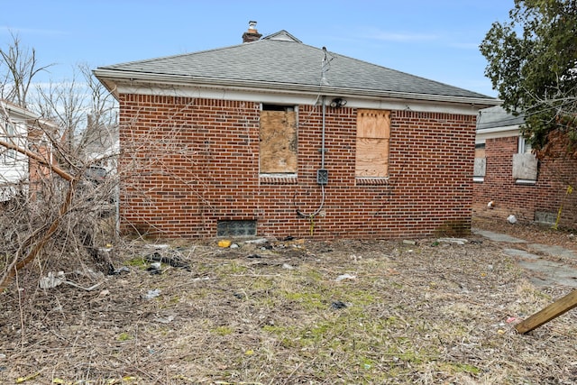 view of side of home with brick siding, roof with shingles, and a chimney