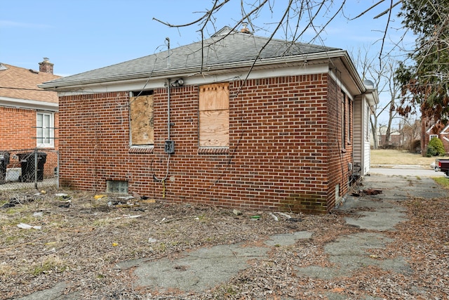 view of side of property with brick siding, roof with shingles, and fence