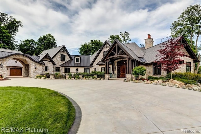 view of front facade with a chimney, concrete driveway, a standing seam roof, metal roof, and stone siding