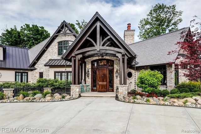 view of front of property featuring stone siding, a standing seam roof, metal roof, and a chimney