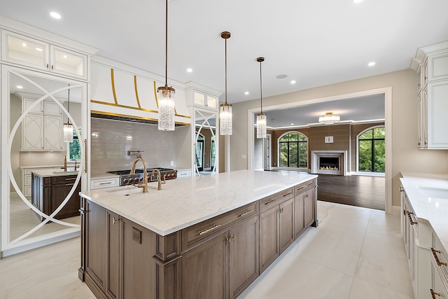 kitchen with a large fireplace, a center island with sink, glass insert cabinets, and decorative light fixtures