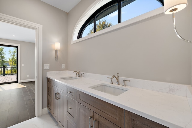 bathroom with marble finish floor, a sink, baseboards, and double vanity