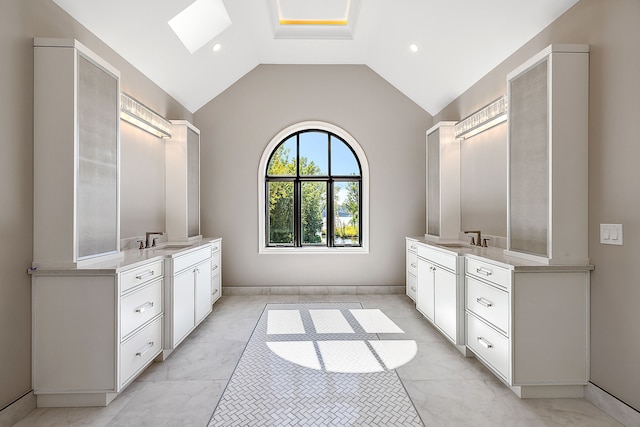 bathroom with marble finish floor, vaulted ceiling with skylight, two vanities, and a sink