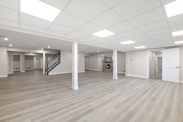 finished basement featuring light wood-style flooring, a fireplace, stairway, and baseboards