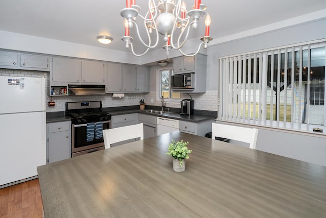 kitchen featuring gray cabinetry, under cabinet range hood, stainless steel appliances, a sink, and dark countertops